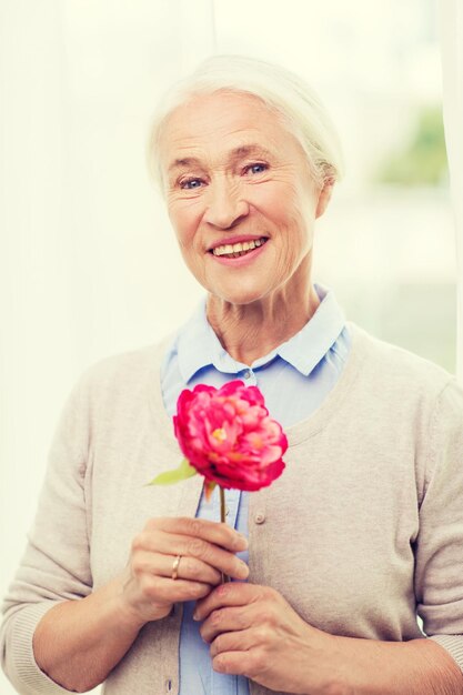 age, holidays and people concept - happy smiling senior woman with flower at home