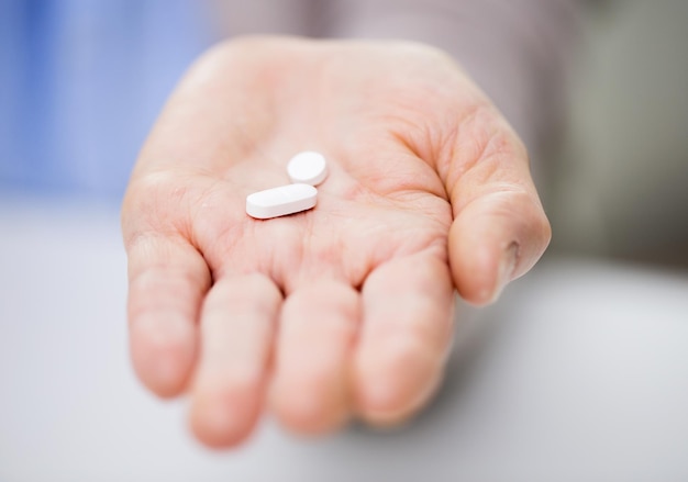 age, medicine, health care and people concept - close up of senior woman cupped hand with pills at home or hospital