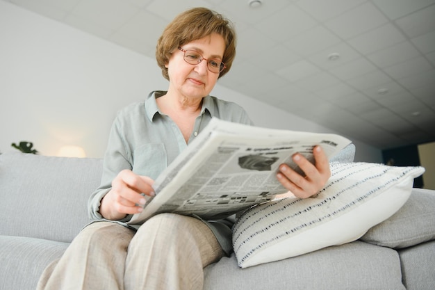 Age and people concept happy senior woman reading newspaper at home