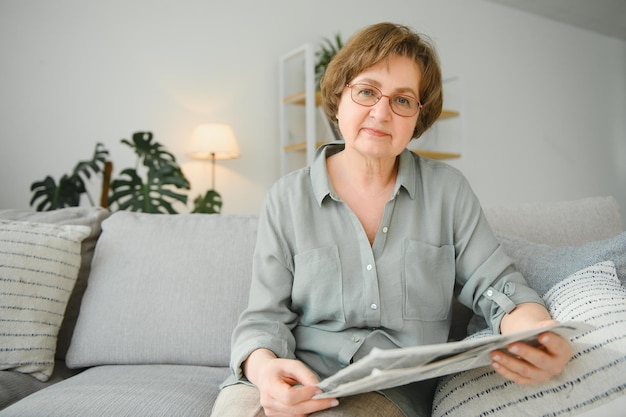 Age and people concept happy senior woman reading newspaper at home