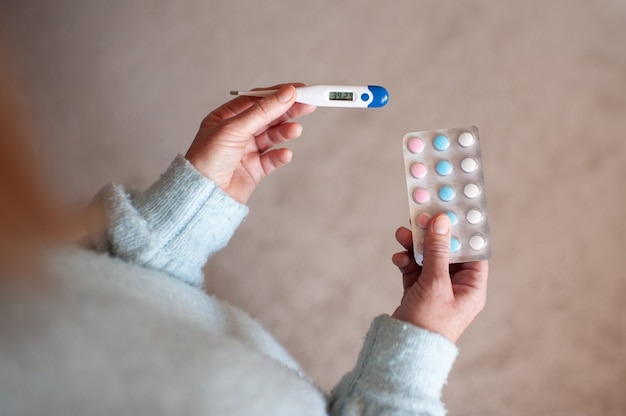 Aged adult woman holding digital thermometer and meds