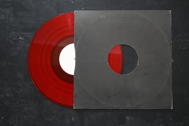 Aged black paper cover and red vinyl LP record isolated on stone background