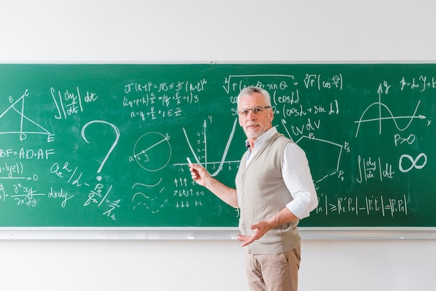 Aged math teacher pointing with chalk at blackboard