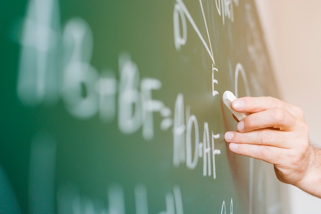 Aged math teacher writing formula on chalkboard