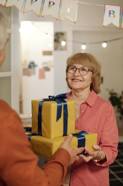 Aged smiling woman in eyeglasses and casualwear taking birthday gift