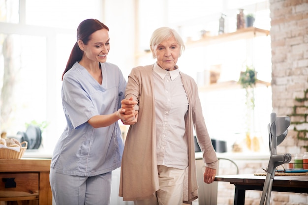 Aged woman walking after surgery with the help of nurse