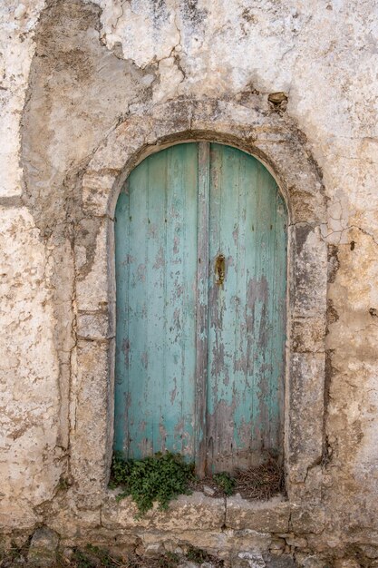 Aged wooden closed peeled door with rusty handle damaged building wall facade Vertical