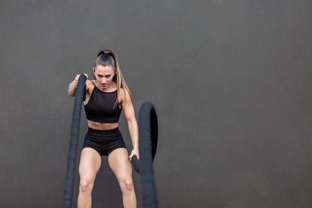 Aggressive sportswoman doing exercise with battle ropes