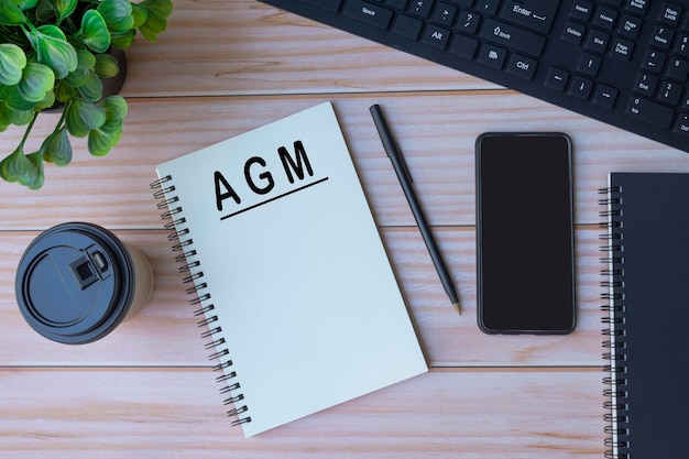 AGM text on notepad with keyboard, pen, coffee and smartphone on wooden table