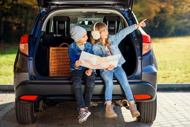 Agreeable boy and girl are looking at the road map while sitting in the auto's trunk and discussing the move direction.