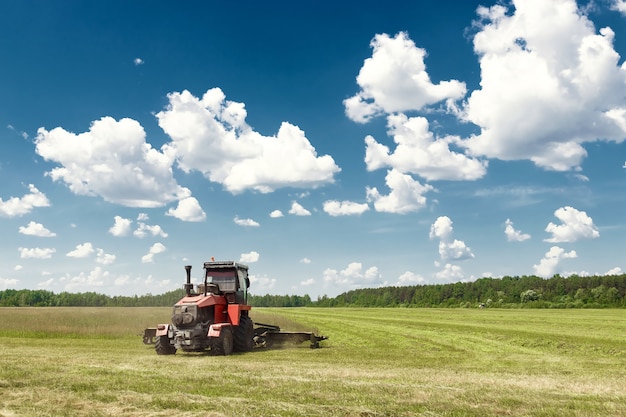 Agricultural machinery, harvester mowing grass in a field against a blue sky