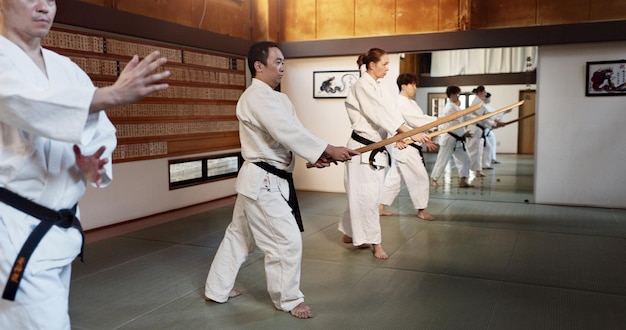 Aikido stick and fight class with weapon training and wooden sword for self defence exercise Dojo students and people in a gym or studio with workout black belt practice and fitness in Japan