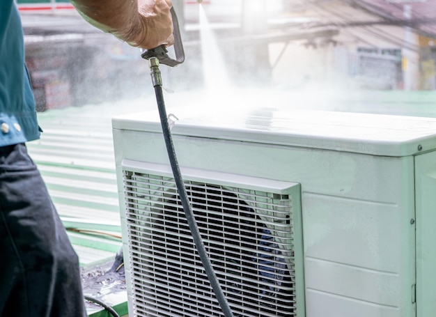 Air conditioner cleaning by a man Technician cleans condensing unit of air conditioner by spraying