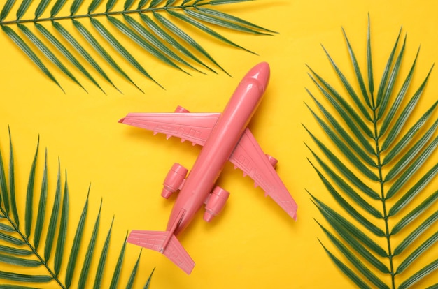 Air plane and palm green leaves on yellow background Travel concept Tropical composition Top view Flat lay