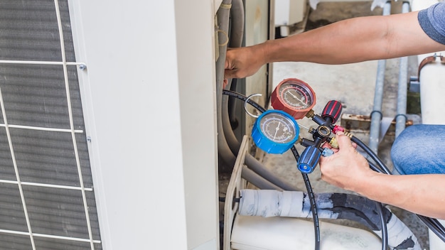 Air repair mechanic using measuring equipment for filling industrial factory air conditioners.