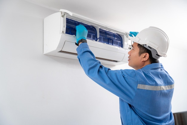 Air technician wearing blue uniform service checking and repairing air conditioner on white wall Service concept of an air conditioner technician