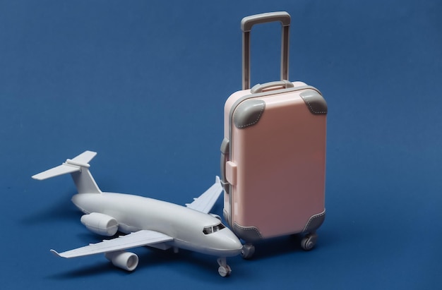 Air travel concept. Mini plastic travel suitcase and air plane on classic blue  background.