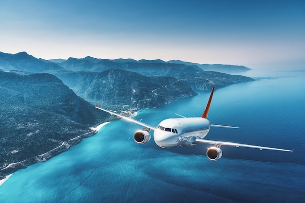 Aircraft is flying over islands and sea at sunrise in summer. Landscape with white passenger airplane