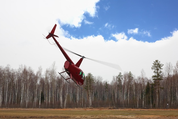 Aircraft the small red helicopter on cloudy sky background