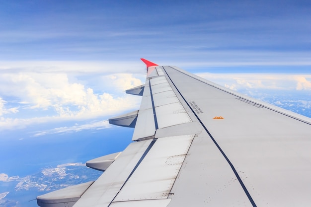 Aircraft wing flying above the clouds in blue sky. from its windows