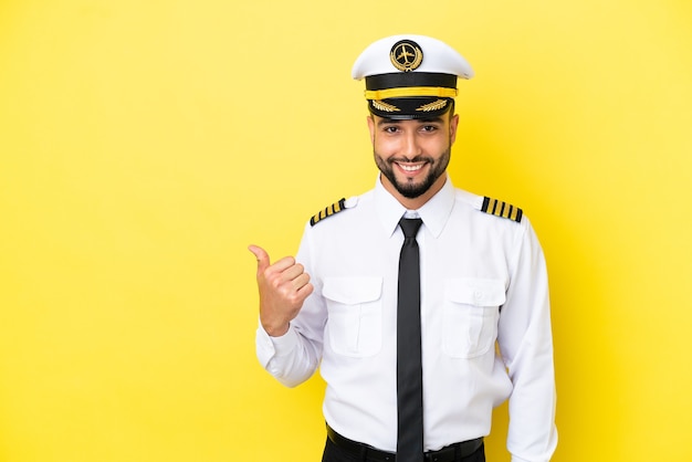 Airplane arab pilot man isolated on yellow background pointing to the side to present a product