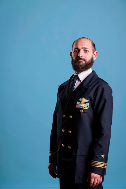 Photo airplane captain standing in professional uniform portrait, confident plane pilot standing, looking at camera, studio medium shot, side view. civil aviator with badge on jacket