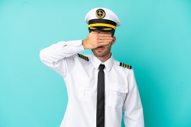 Airplane caucasian pilot isolated on blue background covering eyes by hands. Do not want to see something