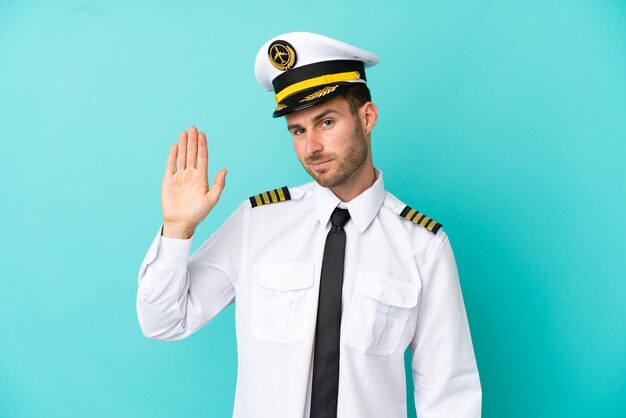 Airplane caucasian pilot isolated on blue background saluting with hand with happy expression