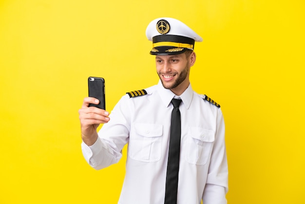 Airplane caucasian pilot isolated on yellow background making a selfie