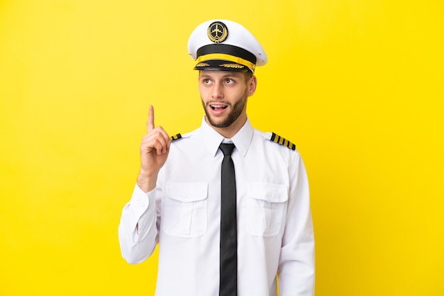 Airplane caucasian pilot isolated on yellow background pointing up and surprised