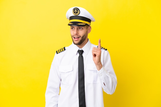 Airplane caucasian pilot isolated on yellow background thinking an idea pointing the finger up