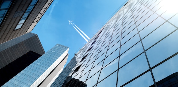 Airplane flying above modern glass buildings skyscraper in financial district of the city