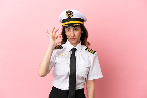 Airplane middle aged pilot woman isolated on pink background showing ok sign with fingers