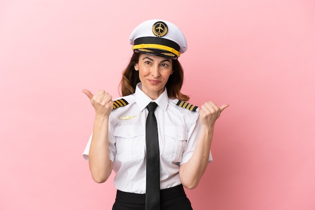 Airplane middle aged pilot woman isolated on pink background with thumbs up gesture and smiling