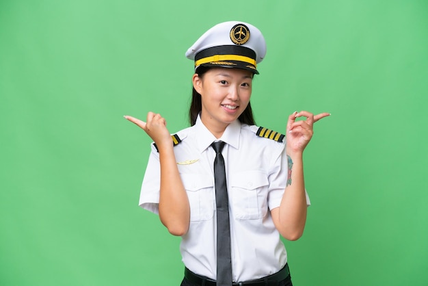 Airplane pilot Asian woman over isolated background pointing finger to the laterals and happy