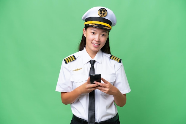 Airplane pilot Asian woman over isolated background sending a message with the mobile