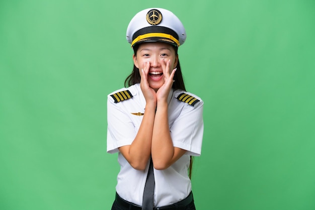 Airplane pilot Asian woman over isolated background shouting and announcing something