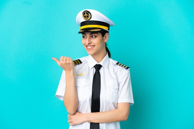 Airplane pilot caucasian woman isolated on blue background pointing to the side to present a product