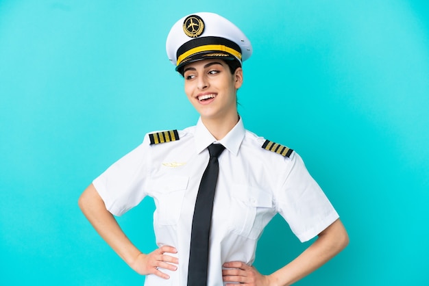 Airplane pilot caucasian woman isolated on blue background posing with arms at hip and smiling