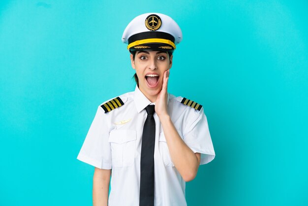 Airplane pilot caucasian woman isolated on blue background with surprise and shocked facial expression