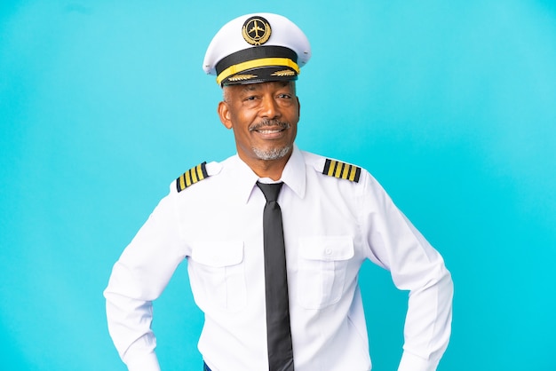 Airplane pilot senior man isolated on blue background posing with arms at hip and smiling