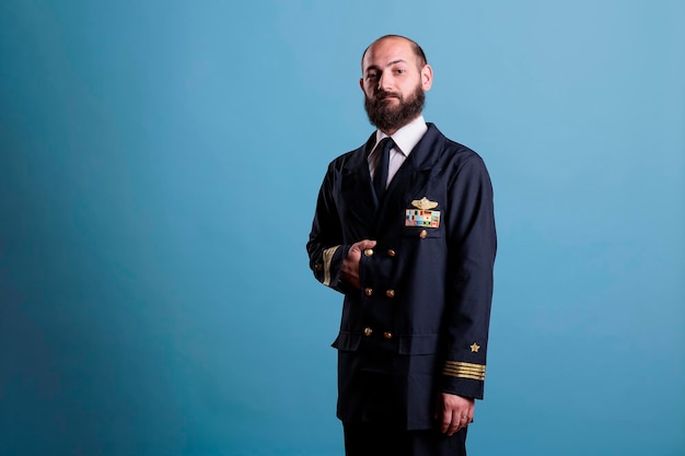 Airplane pilot wearing uniform portrait, confident plane captain standing, looking at camera, studio medium shot. Serious handsome aviator with badge on professional suit