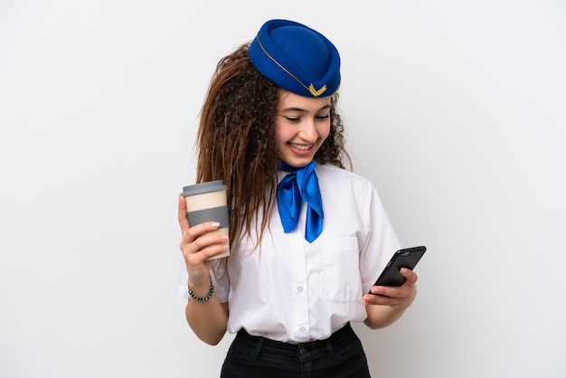 Airplane stewardess Arab woman isolated on white background holding coffee to take away and a mobile