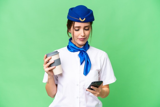 Airplane stewardess over isolated chroma key background holding coffee to take away and a mobile