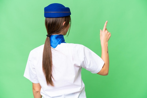 Airplane stewardess over isolated chroma key background pointing back with the index finger