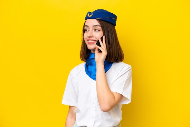 Airplane stewardess Ukrainian woman isolated on yellow background keeping a conversation with the mobile phone with someone