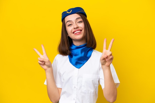 Airplane stewardess Ukrainian woman isolated on yellow background showing victory sign with both hands