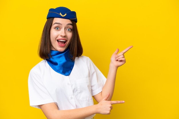 Airplane stewardess Ukrainian woman isolated on yellow background surprised and pointing side