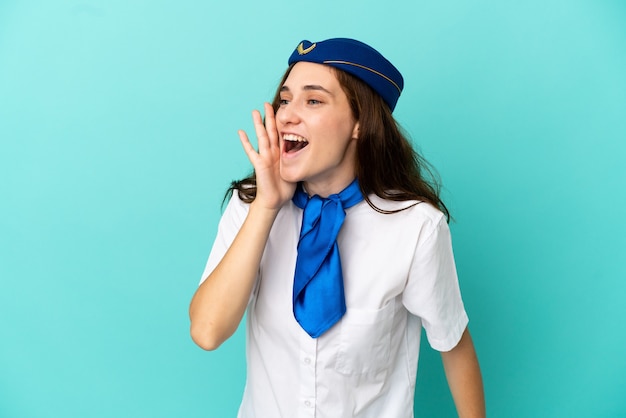 Airplane stewardess woman isolated on blue background shouting with mouth wide open to the lateral