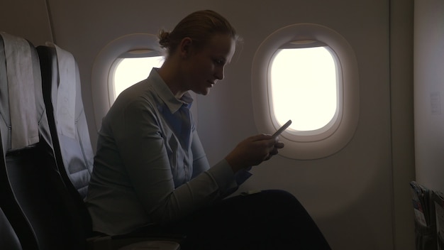 In airplane view of woman making payment with bank card using smartphone and dongle for scanning ban...